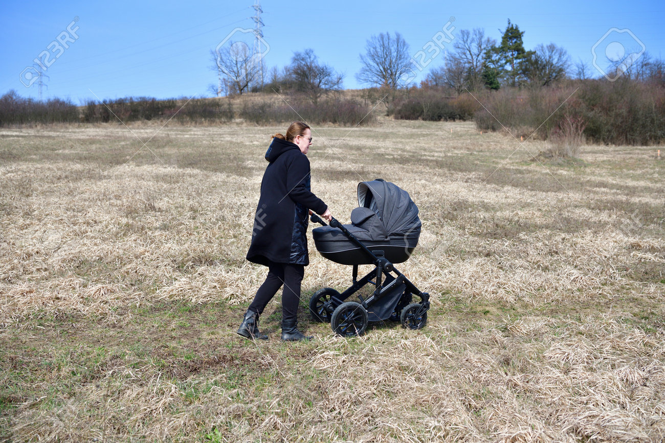 A woman dressed in a black coat on a walk with a baby carriage in the spring nature - 168381668 A woman dressed in a black coat on a walk with a baby carriage in the spring nature - 168381668