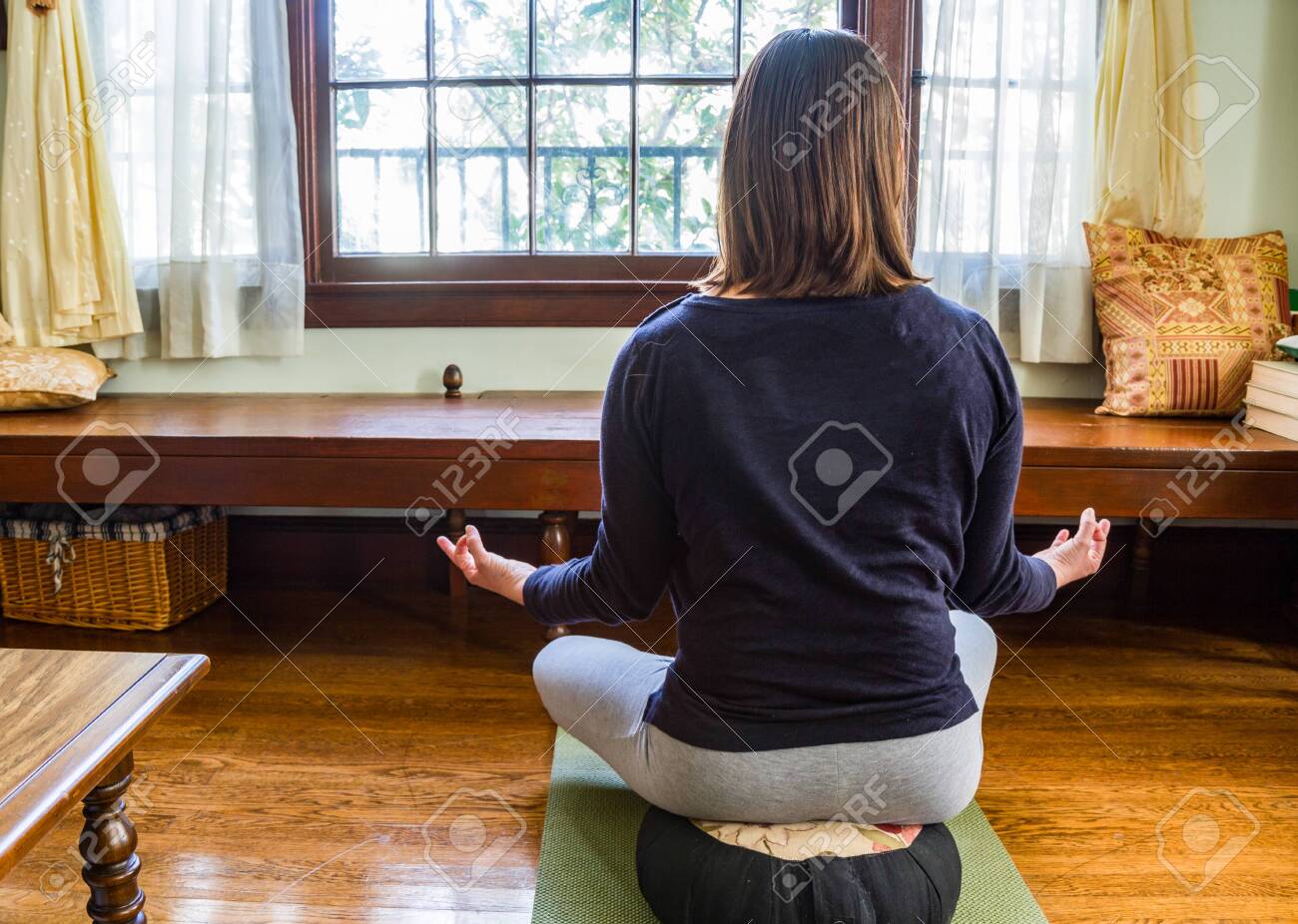 Young Woman Sitting In Mediation Pose On Cushion On Wood Floor