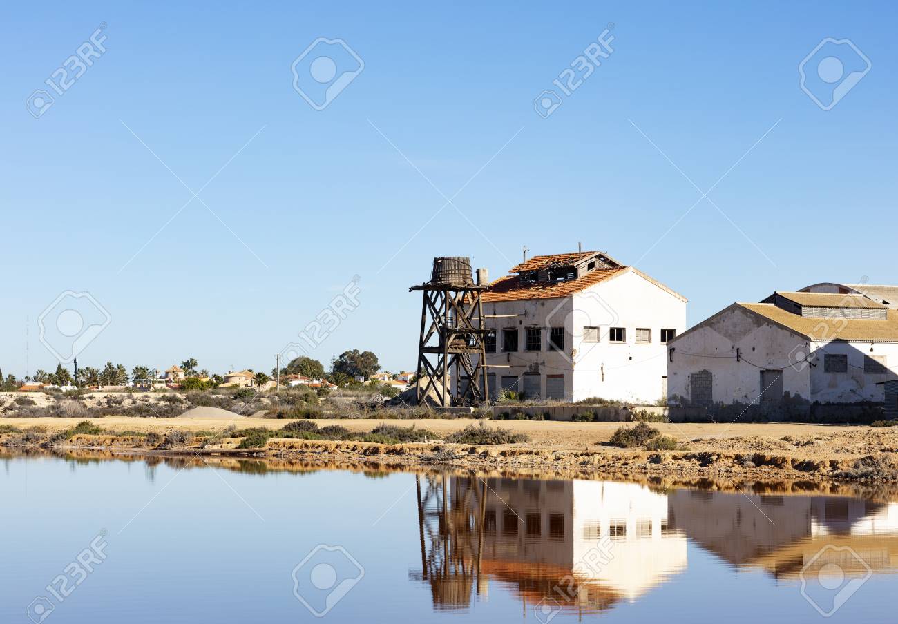 old ruined building with wooden water tank on the edge of a saline lake, both are reflected in the water on the blue background of the sky - 116921200 old ruined building with wooden water tank on the edge of a saline lake, both are reflected in the water on the blue background of the sky - 116921200