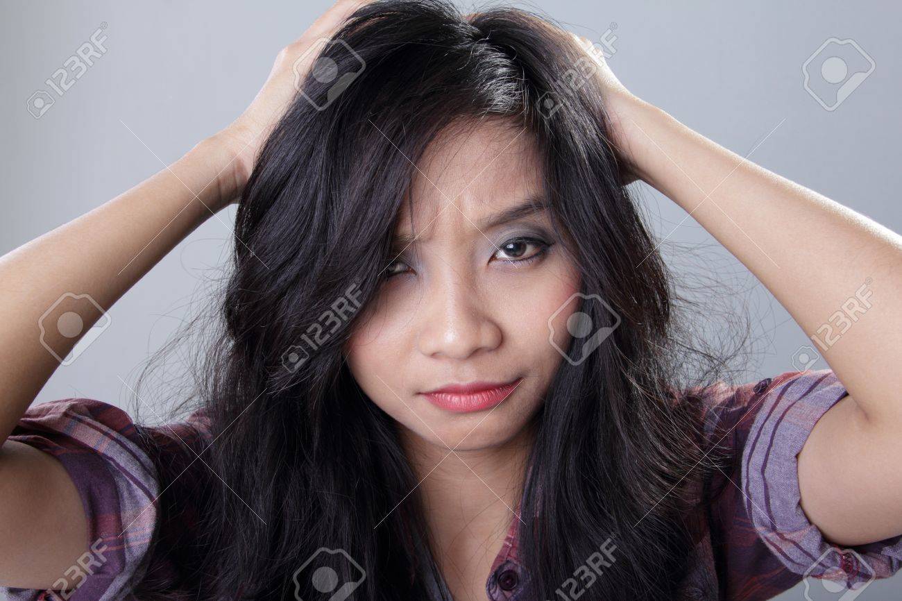 灰色の背景にカメラを見ながら両手で彼女の髪を引っ張って欲求不満な女の顔 の写真素材 画像素材 Image