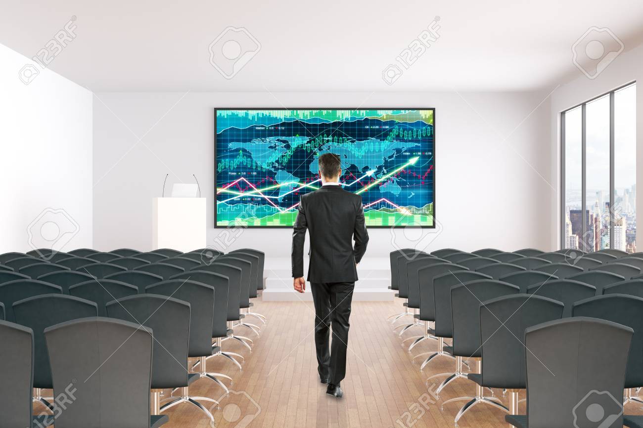 Download Businessman Walking Towards Board With Forex Chart In Conference Hall Interior With Rows Of Seats Wooden Floor Concrete Walls And Window With City View Mock Up 3d Rendering Stock Photo Picture And