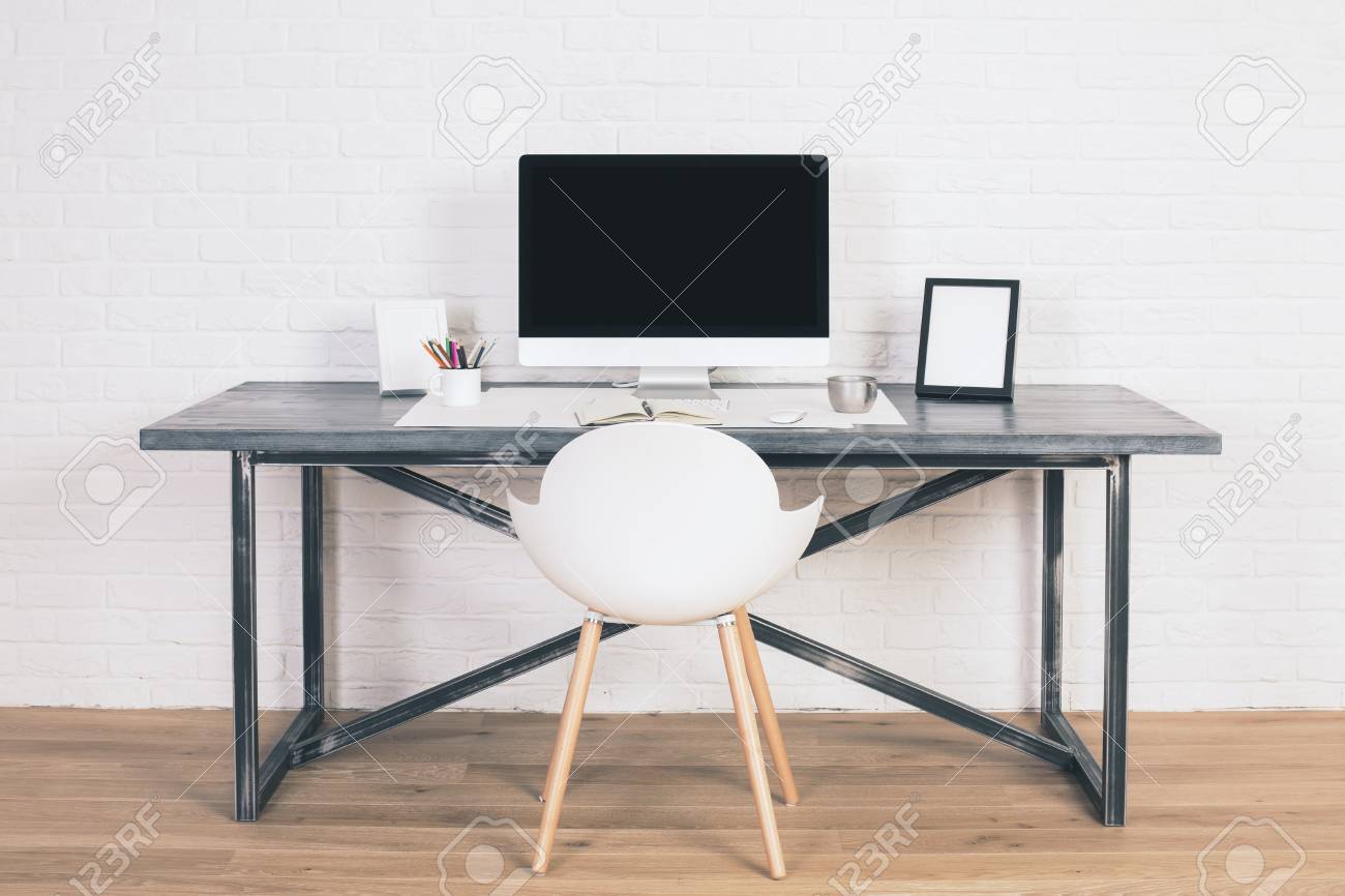 Front View Of Designer Desk With Blank Computer Monitor, Frames And Other  Items With White Chair Next To It. Wooden Floor And White Brick Wall  Background. Mock Up Stock Photo, Picture and, image size:1300x866