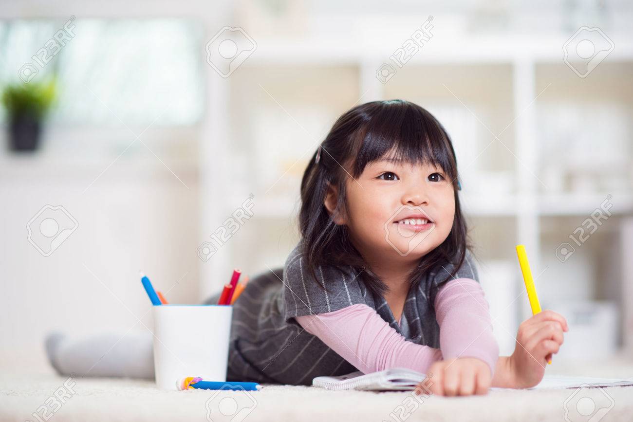 Pretty happy little japanese girl lying and drawing with pencils on white capet at home - 70370635 Pretty happy little japanese girl lying and drawing with pencils on white capet at home - 70370635