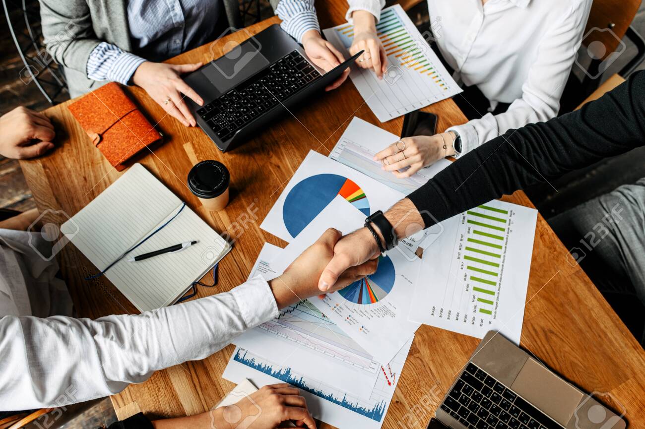 The result of a successful meeting. Top view of men shaking hands above papers with graphs and diagrams, their faces are not visible - 139904600 The result of a successful meeting. Top view of men shaking hands above papers with graphs and diagrams, their faces are not visible - 139904600