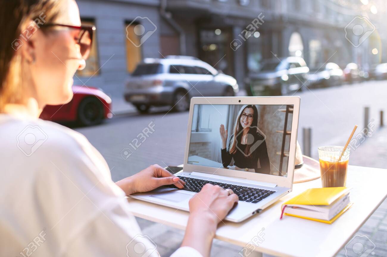 Virtual meeting with a friend. Young woman sits at the table in the street cafe and uses laptop for video call to another woman, two female friends are talking online - 149643513 Virtual meeting with a friend. Young woman sits at the table in the street cafe and uses laptop for video call to another woman, two female friends are talking online - 149643513