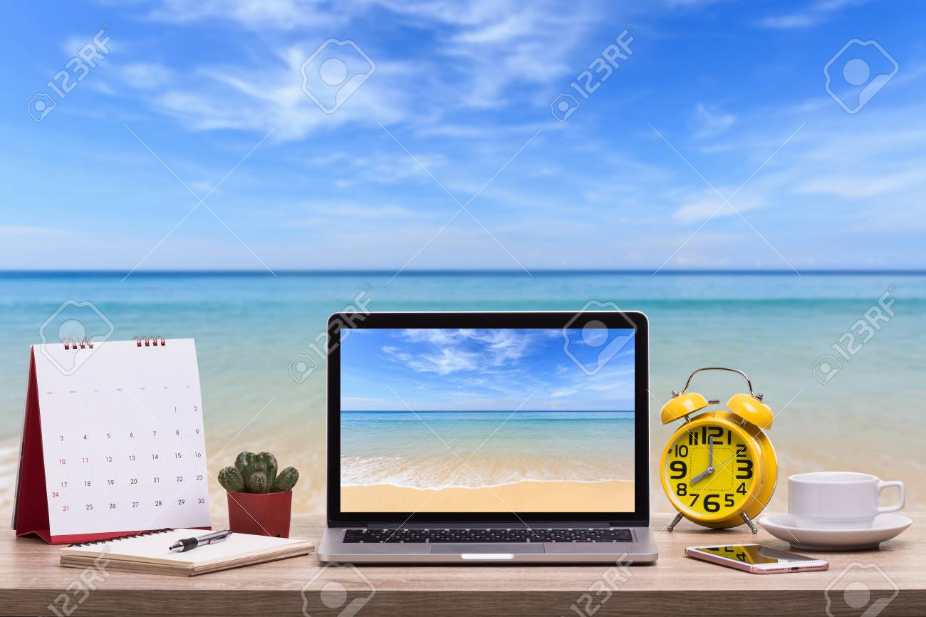 Modern laptop computer, Coffee cup, alarm clock, notebook and calendar on wooden table and view of tropical beach background. - 97014015 Modern laptop computer, Coffee cup, alarm clock, notebook and calendar on wooden table and view of tropical beach background. - 97014015