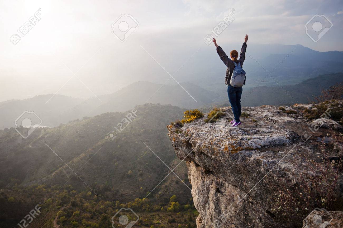 両腕と崖の上に立って、渓谷の景色を楽しんでいる若い女性の写真素材