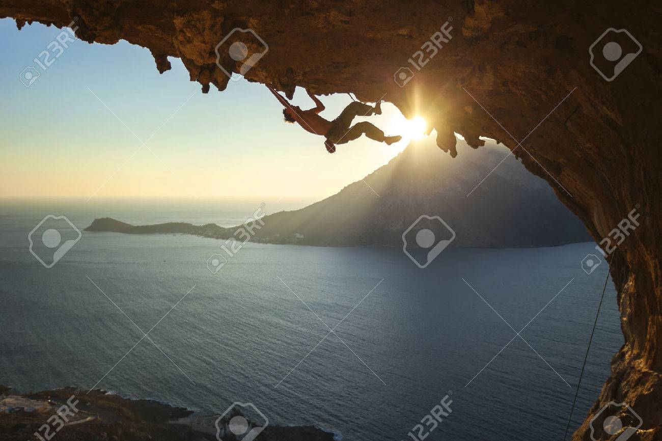 Male rock climber climbing along a roof in a cave at sunset - 49280873 Male rock climber climbing along a roof in a cave at sunset - 49280873