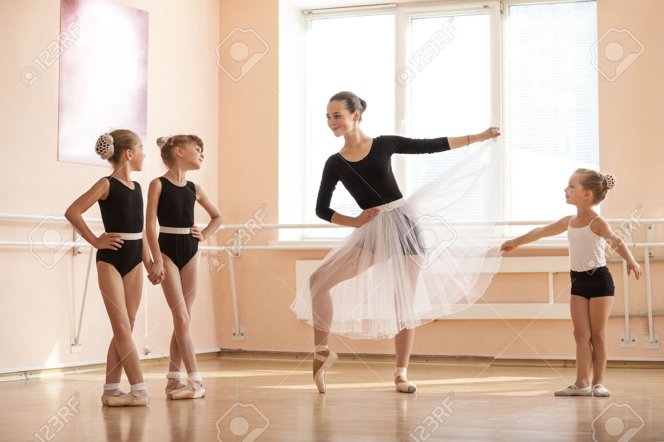 Young girl warming up and talking to younger classmates at ballet dancing class - 48996591 Young girl warming up and talking to younger classmates at ballet dancing class - 48996591