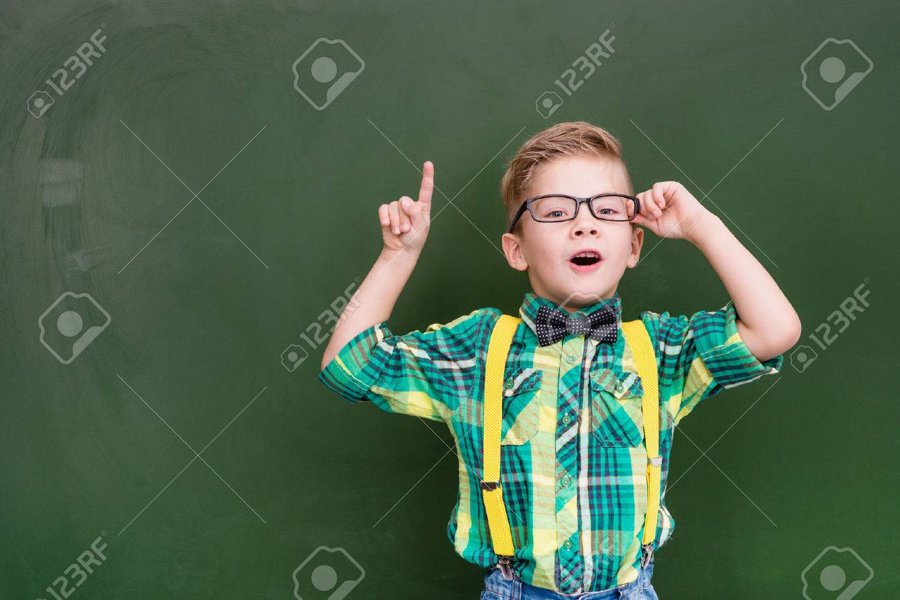 Surprised boy stands near empty chalkboard and showing finger up. - 51089497 Surprised boy stands near empty chalkboard and showing finger up. - 51089497