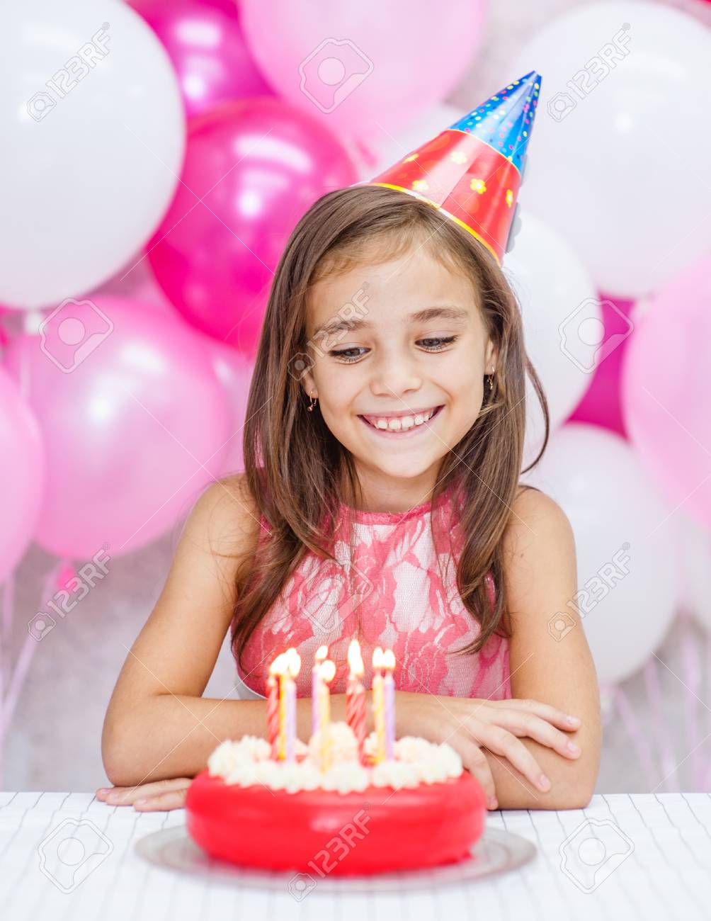 バースデーケーキを見ているパーティーハットで幸せな女の子 の写真素材 画像素材 Image