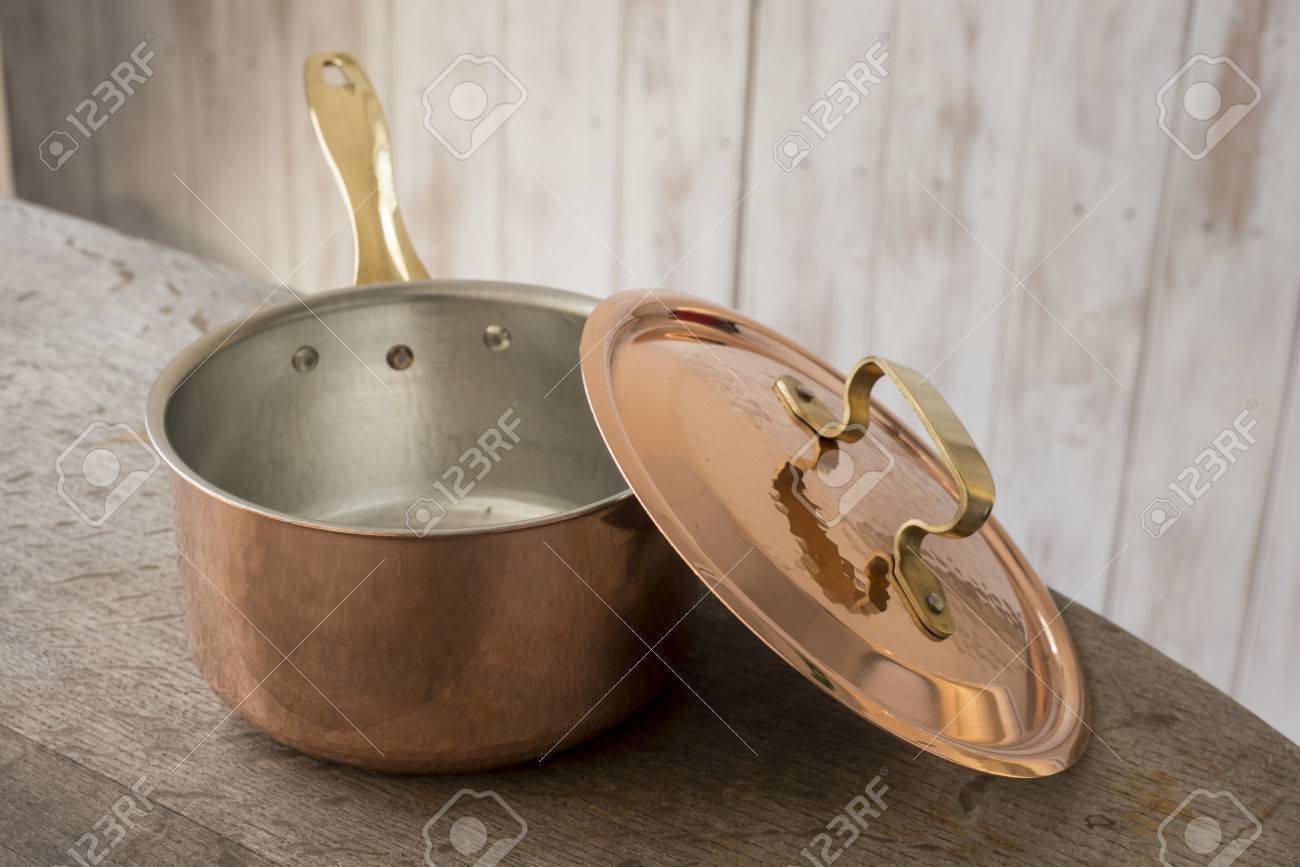 Una cacerola de cobre vacía con tapa inclinado sobre su lado y se coloca en una encimera de madera. Una cacerola de cobre vacía con tapa inclinado sobre su lado y se coloca en una encimera de madera.