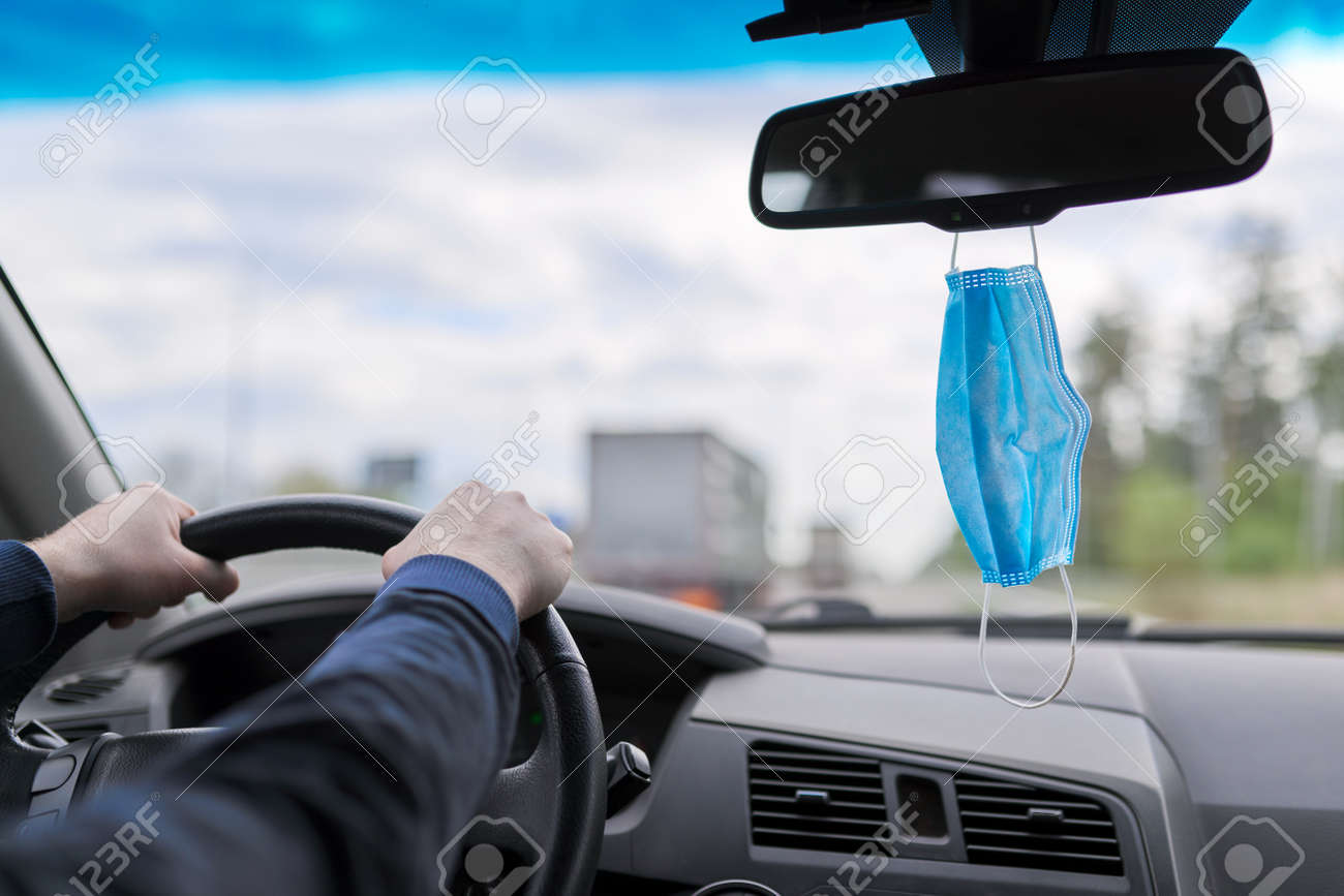 Protective medical mask of the driver in the car, man's hands on the steering wheel of moving vehicle - 155423815 Protective medical mask of the driver in the car, man's hands on the steering wheel of moving vehicle - 155423815