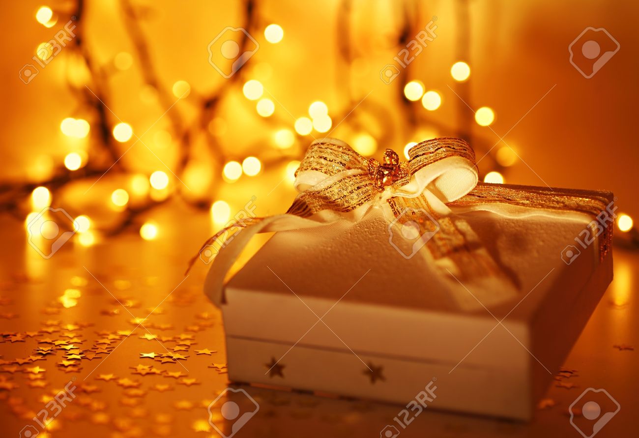 Gold holiday background with white present gift box, Christmas ornament and new year decoration over defocused lights - 8323874 Gold holiday background with white present gift box, Christmas ornament and new year decoration over defocused lights - 8323874