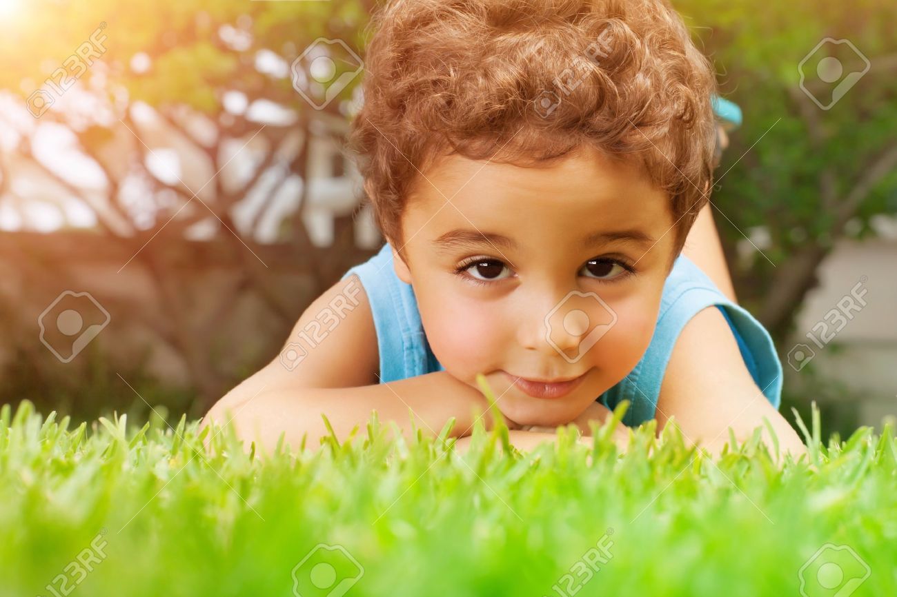 Closeup Portrait Of Cute Arabic Little Boy Lying Down On Green
