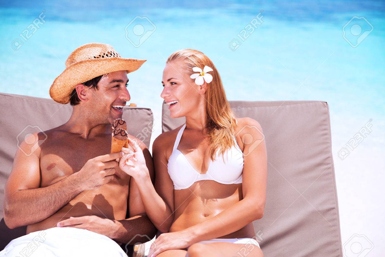 Happy Couple Sur La Plage Assis Sur Des Lits De Bronzage Et De Manger La Crème Glacée Savoureuse Douce Avec Lamour En Regardant Les Uns Les Autres