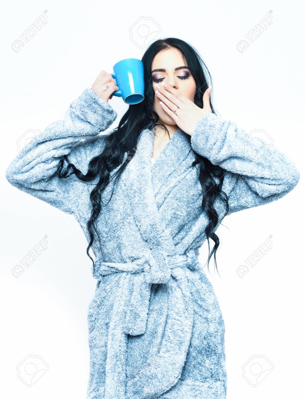 かなりあくび眠いかわいいセクシーな女の子やファッションメイク 白い背景で隔離のカップで青いベロア バスローブでポーズ巻き 長い髪の美女 の写真素材 画像素材 Image