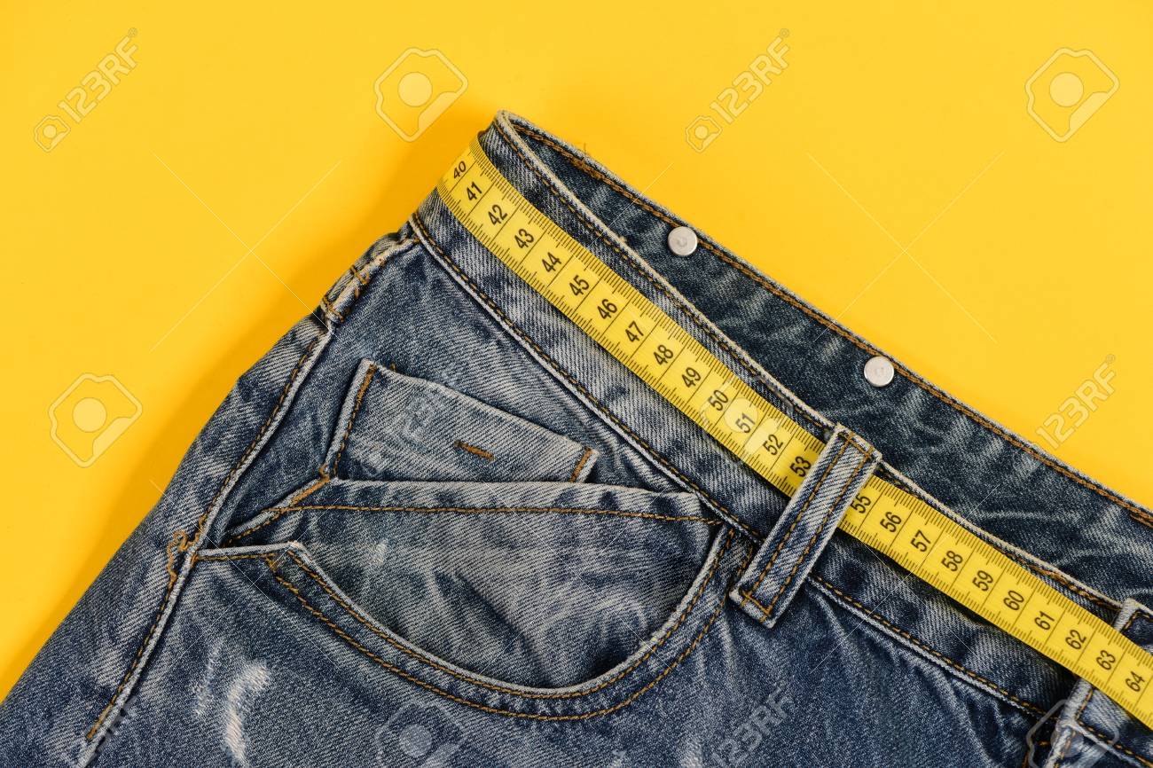 ジーンズのベルトループやポケットのクローズ アップ ベルトの代わりに黄色のメジャー テープ付きジーンズ 健康的なライフ スタイルとダイエットのコンセプト 黄色の背景に分離されたデニムのズボンの上の部分 の写真素材 画像素材 Image