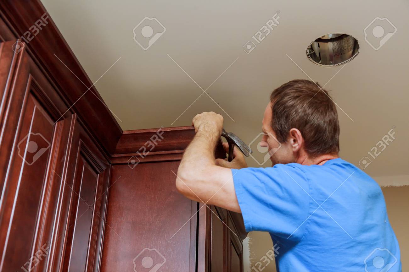 Carpenter Brad Using Nail Gun To Crown Moulding On Kitchen