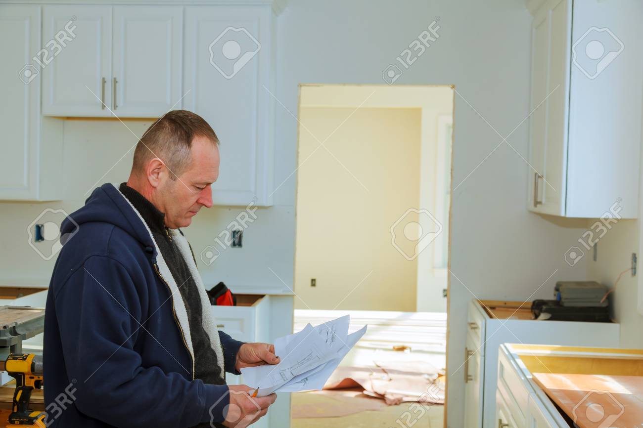 The Worker Keeps A Plan For Installing The Kitchen Cabinets