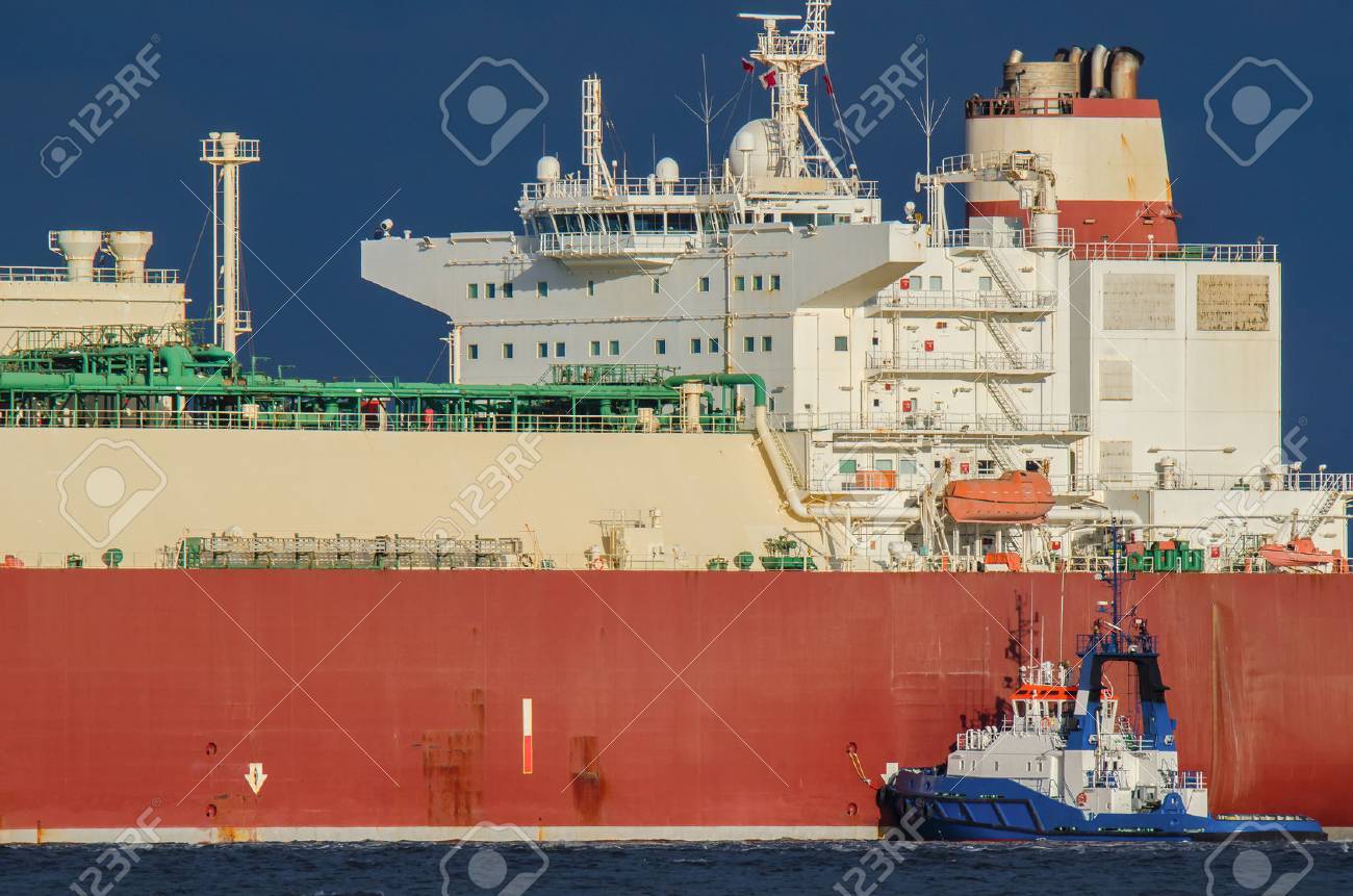 SWINOUJSCIE. Small tugboat helps to moor at the quay big lng tanker - 61547101 SWINOUJSCIE. Small tugboat helps to moor at the quay big lng tanker - 61547101