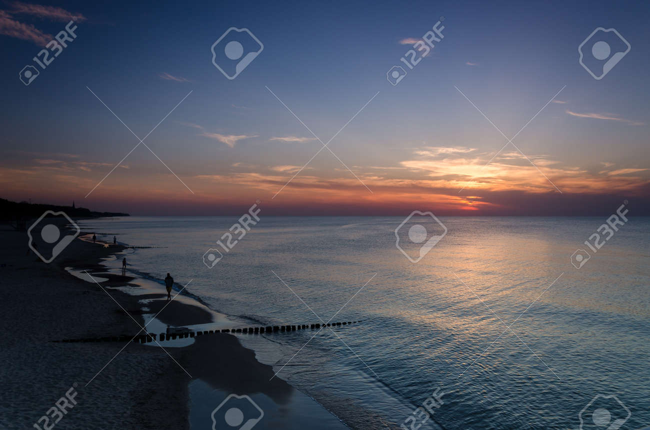 SUNSET OVER THE SEASHORE - People are walking on the beach - 169541029 SUNSET OVER THE SEASHORE - People are walking on the beach - 169541029