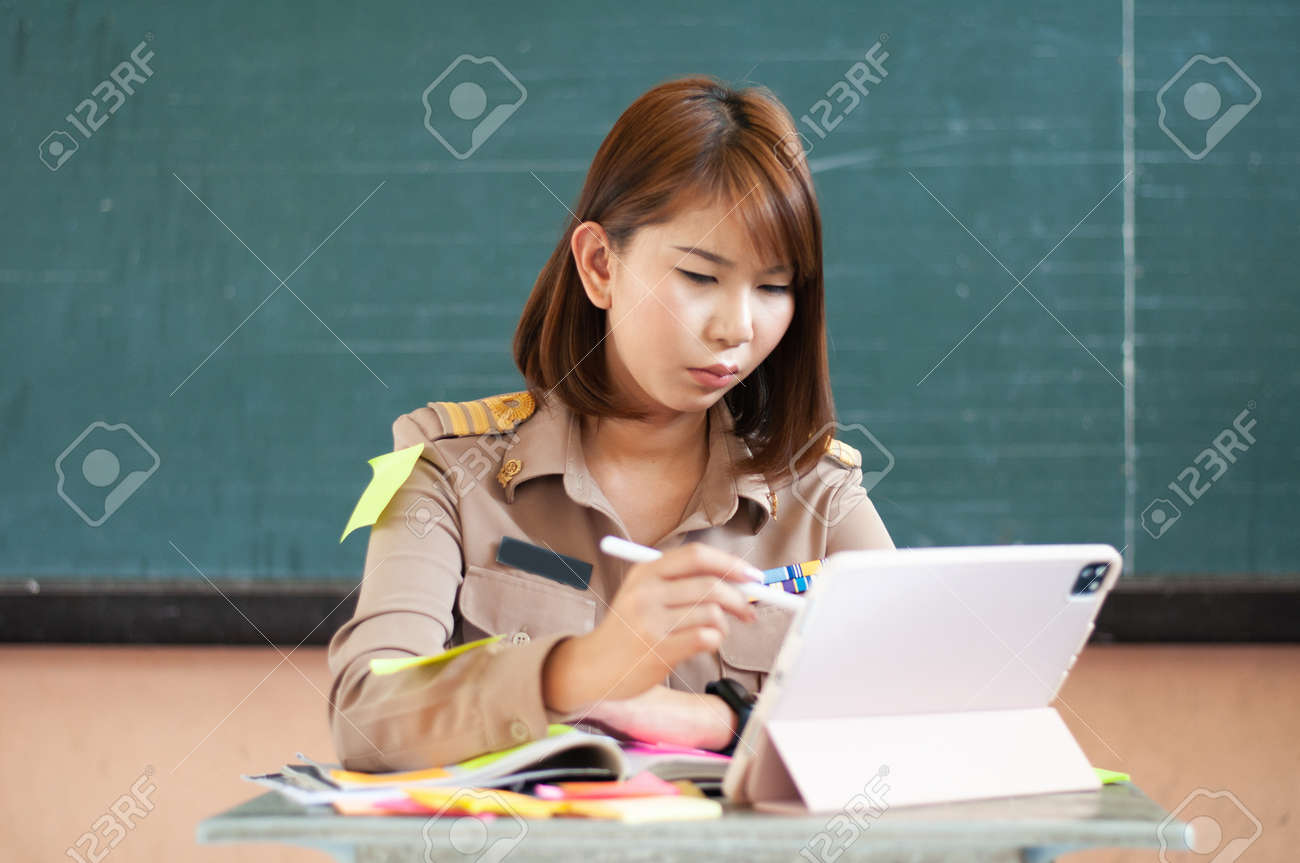 Female Thai teacher holding notebook to the computer while smiling - 166602849 Female Thai teacher holding notebook to the computer while smiling - 166602849