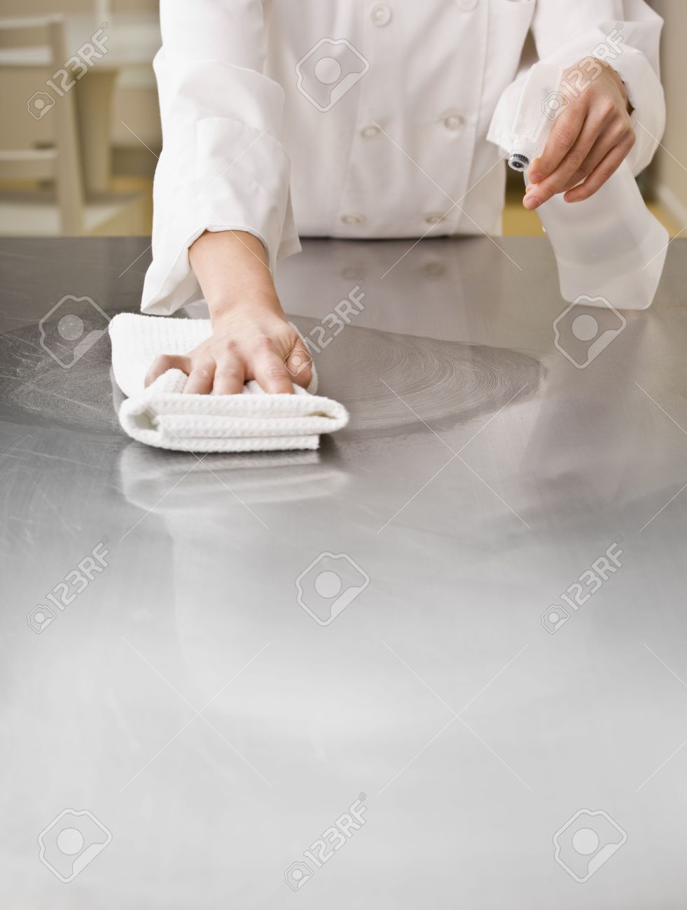 A chef is cleaning a counter in a professional kitchen with a bottle of solution and a rag. Vertically framed shot. - 5333254 A chef is cleaning a counter in a professional kitchen with a bottle of solution and a rag. Vertically framed shot. - 5333254