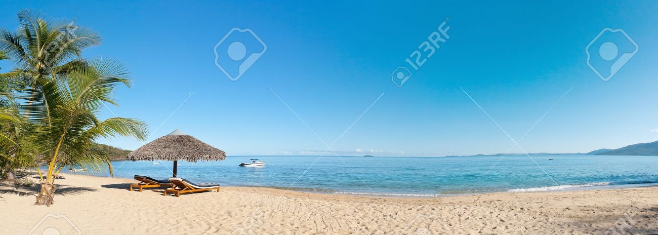 Tropical beach panorama with deckchairs, umbrellas, boats and palm tree - 7396645 Tropical beach panorama with deckchairs, umbrellas, boats and palm tree - 7396645