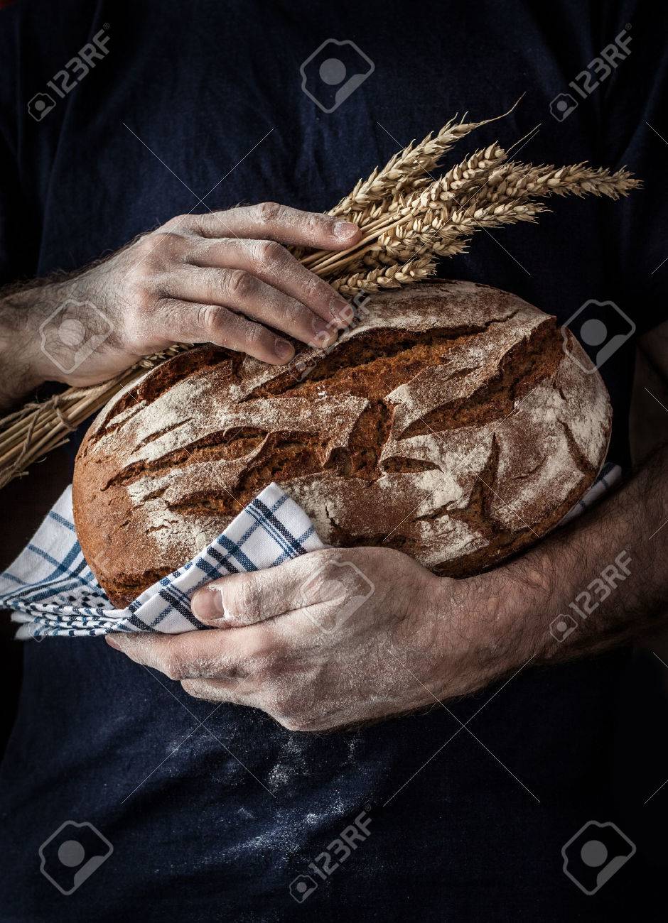 Baker man holding rustic organic loaf of bread and wheat in hands - rural bakery. Natural light, moody still life with free text space good for cover or poster. - 55317382 Baker man holding rustic organic loaf of bread and wheat in hands - rural bakery. Natural light, moody still life with free text space good for cover or poster. - 55317382