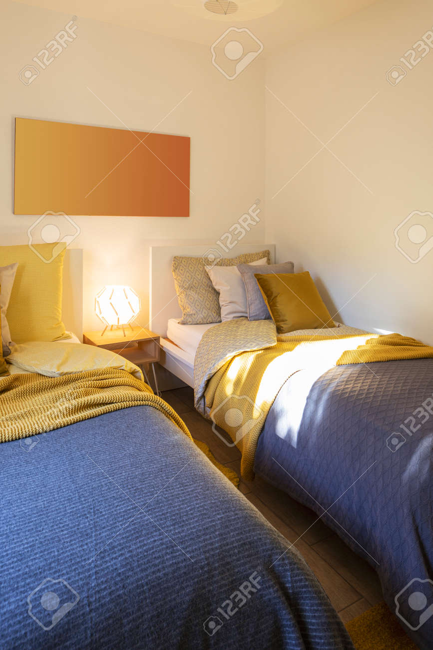 Modern bedroom with two singles beds with clean bed sheets and large pillow above. White wall. Nobody inside. - 163075636 Modern bedroom with two singles beds with clean bed sheets and large pillow above. White wall. Nobody inside. - 163075636