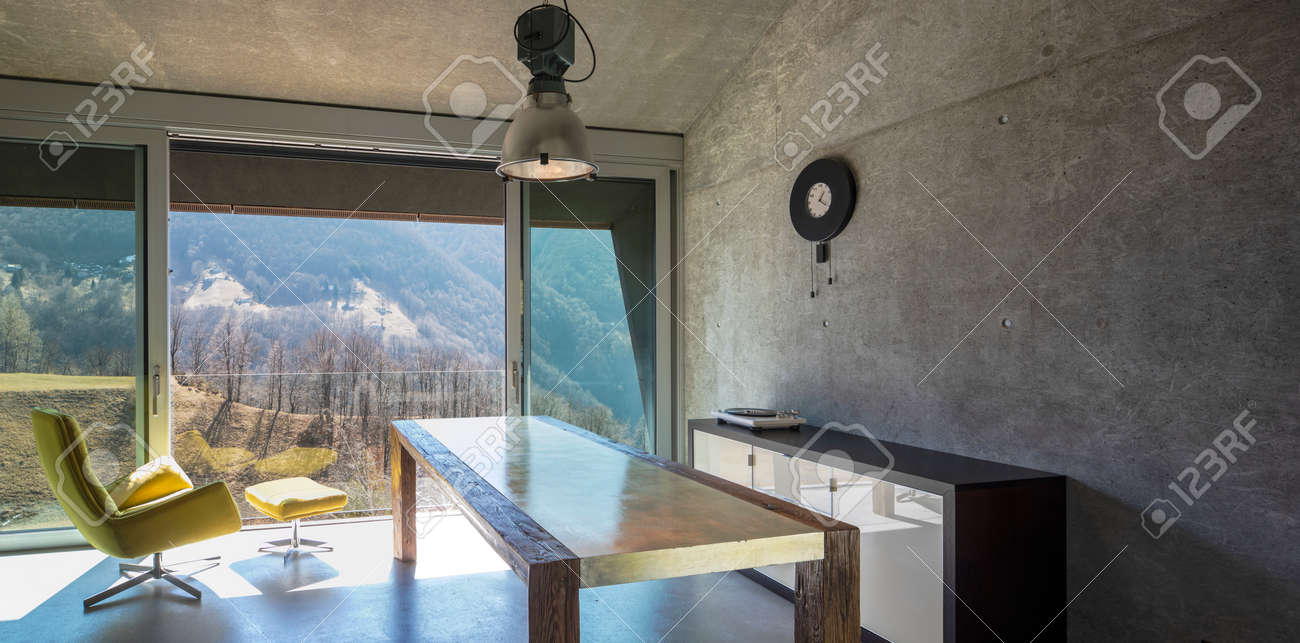 Interior of a beautiful modern house, where you see a table, a yellow armchair and a view of nature. None inside - 166417751 Interior of a beautiful modern house, where you see a table, a yellow armchair and a view of nature. None inside - 166417751