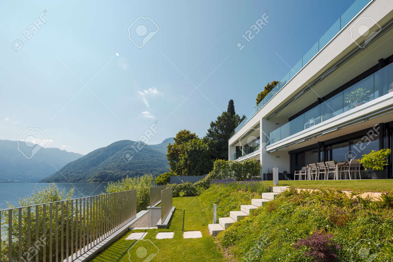 Modern house of two apartments with a beautiful garden directly on Lake Ceresio. Sunny day with blue sky. Minimalist and linear architecture. Panoramic view of the lake. Space for your text - 171413590 Modern house of two apartments with a beautiful garden directly on Lake Ceresio. Sunny day with blue sky. Minimalist and linear architecture. Panoramic view of the lake. Space for your text - 171413590