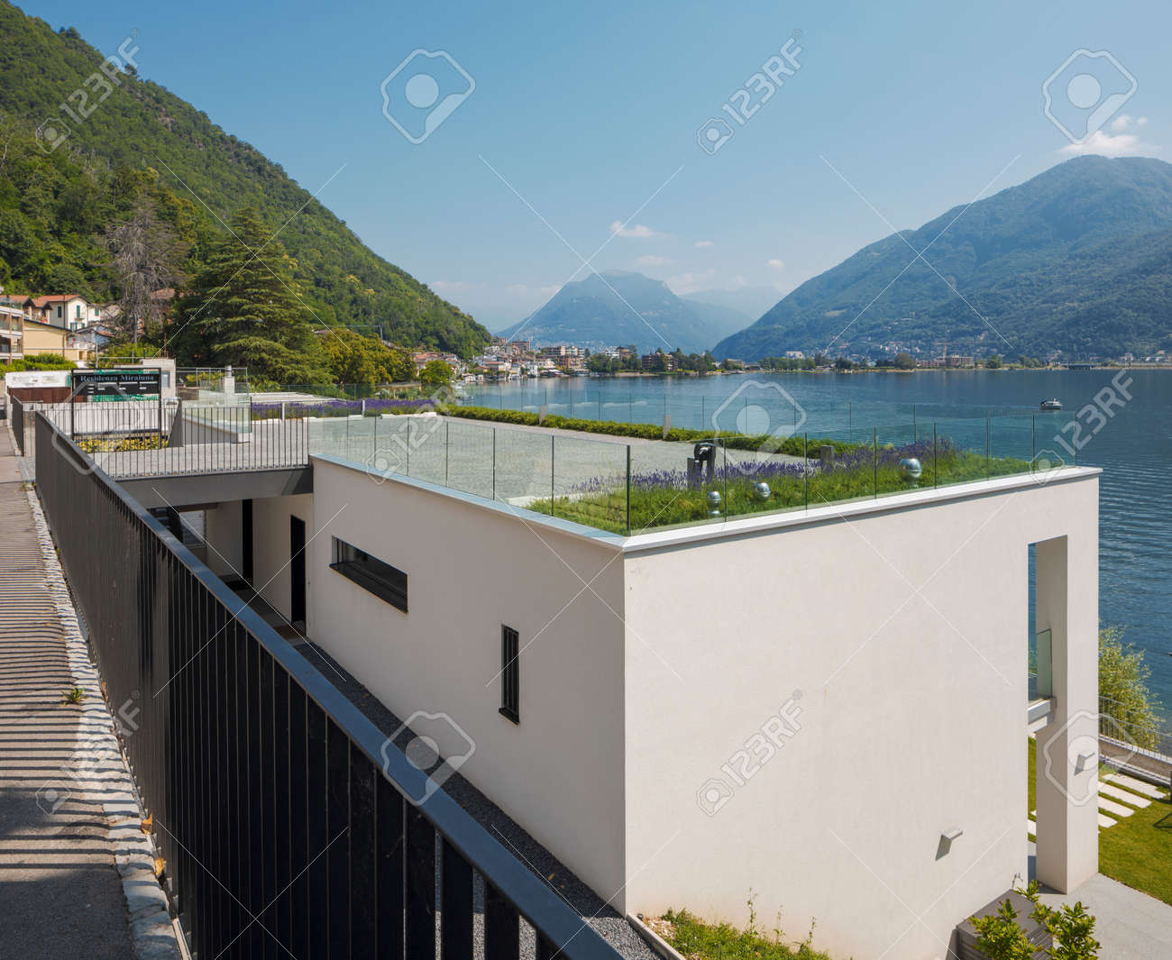 Behind modern house with rooftop parking and lavender. House with lake and mountain views. Sunny summer day. Nobody inside - 171412965 Behind modern house with rooftop parking and lavender. House with lake and mountain views. Sunny summer day. Nobody inside - 171412965