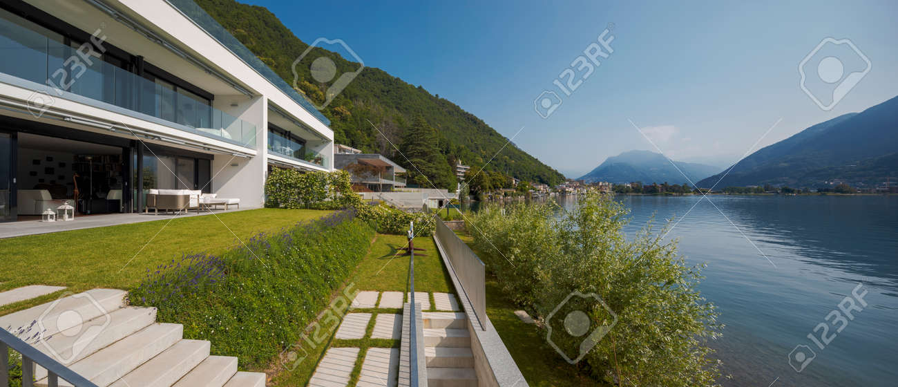 Modern house of two apartments with a beautiful garden directly on Lake Ceresio. Sunny day with blue sky. Minimalist and linear architecture. Panoramic view of the lake. Space for your text - 171413036 Modern house of two apartments with a beautiful garden directly on Lake Ceresio. Sunny day with blue sky. Minimalist and linear architecture. Panoramic view of the lake. Space for your text - 171413036