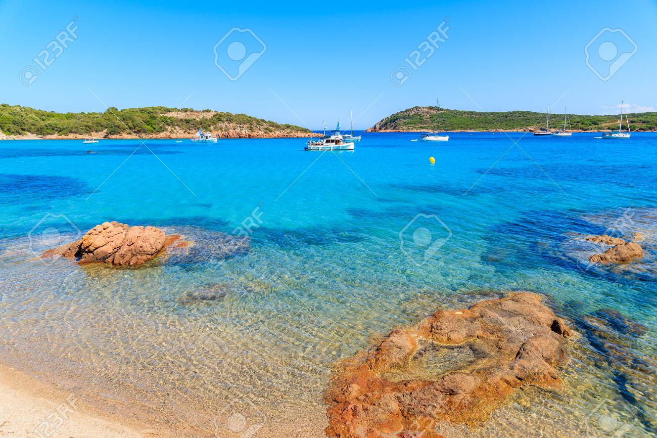 Red Color Rocks On Santa Giulia Beach With Boats On Azure Sea