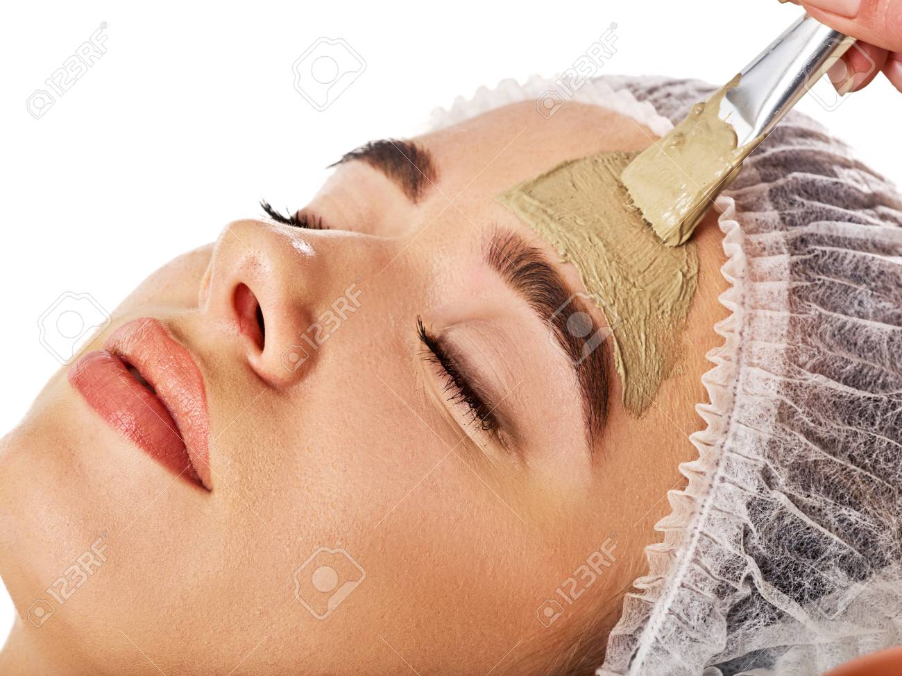 Mud facial mask of woman in spa salon. Massage with clay full face. Girl on with therapy room. Beautician with brush therapeutic procedure isolated background. Healing clay for face. Facelift. - 102254003 Mud facial mask of woman in spa salon. Massage with clay full face. Girl on with therapy room. Beautician with brush therapeutic procedure isolated background. Healing clay for face. Facelift. - 102254003