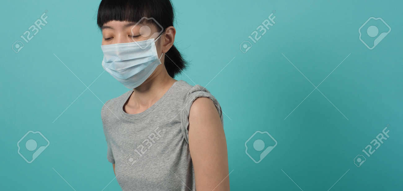 Vaccine Concept. Woman waiting for coronavirus vaccine injection by doctor. Asian woman with medical mask open shoulder and upper arm on blue green background. Waiting for vaccination. - 168300452 Vaccine Concept. Woman waiting for coronavirus vaccine injection by doctor. Asian woman with medical mask open shoulder and upper arm on blue green background. Waiting for vaccination. - 168300452