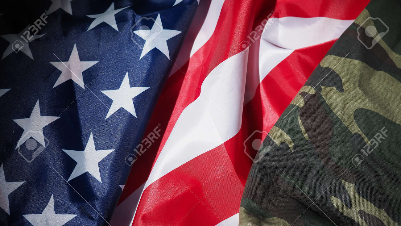 Military hat or bag laying with american flag. Soldier hat or helmet with national american flag on black background. Represent military concept by camouflage object and USA nation flag. - 170416253 Military hat or bag laying with american flag. Soldier hat or helmet with national american flag on black background. Represent military concept by camouflage object and USA nation flag. - 170416253
