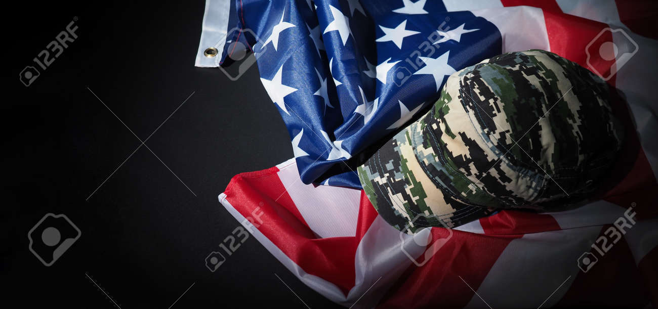 Military hat or bag laying with american flag. Soldier hat or helmet with national american flag on black background. Represent military concept by camouflage object and USA nation flag. - 170416256 Military hat or bag laying with american flag. Soldier hat or helmet with national american flag on black background. Represent military concept by camouflage object and USA nation flag. - 170416256