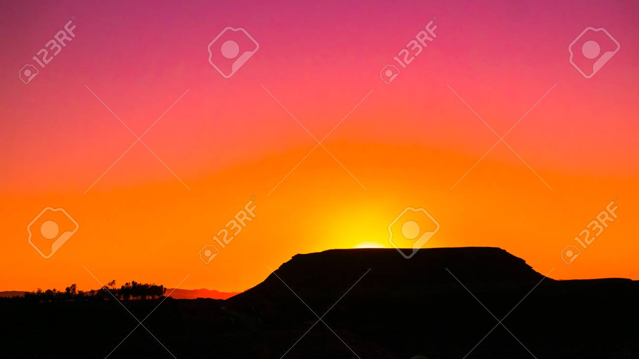 Sun slowly fading behind the mountain in the distance - 58641320 Sun slowly fading behind the mountain in the distance - 58641320