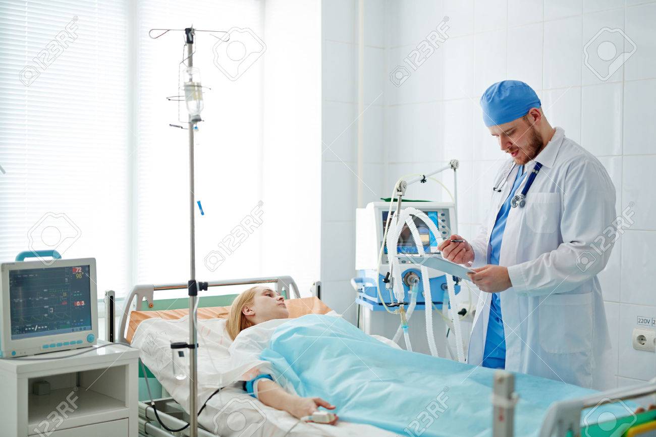 Doctor standing at bed with patient in intensive care - 56140256 Doctor standing at bed with patient in intensive care - 56140256