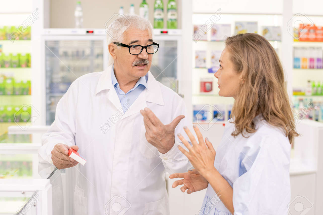 Senior male pharmacist holding new medicaments while consulting his assistant - 155627611 Senior male pharmacist holding new medicaments while consulting his assistant - 155627611
