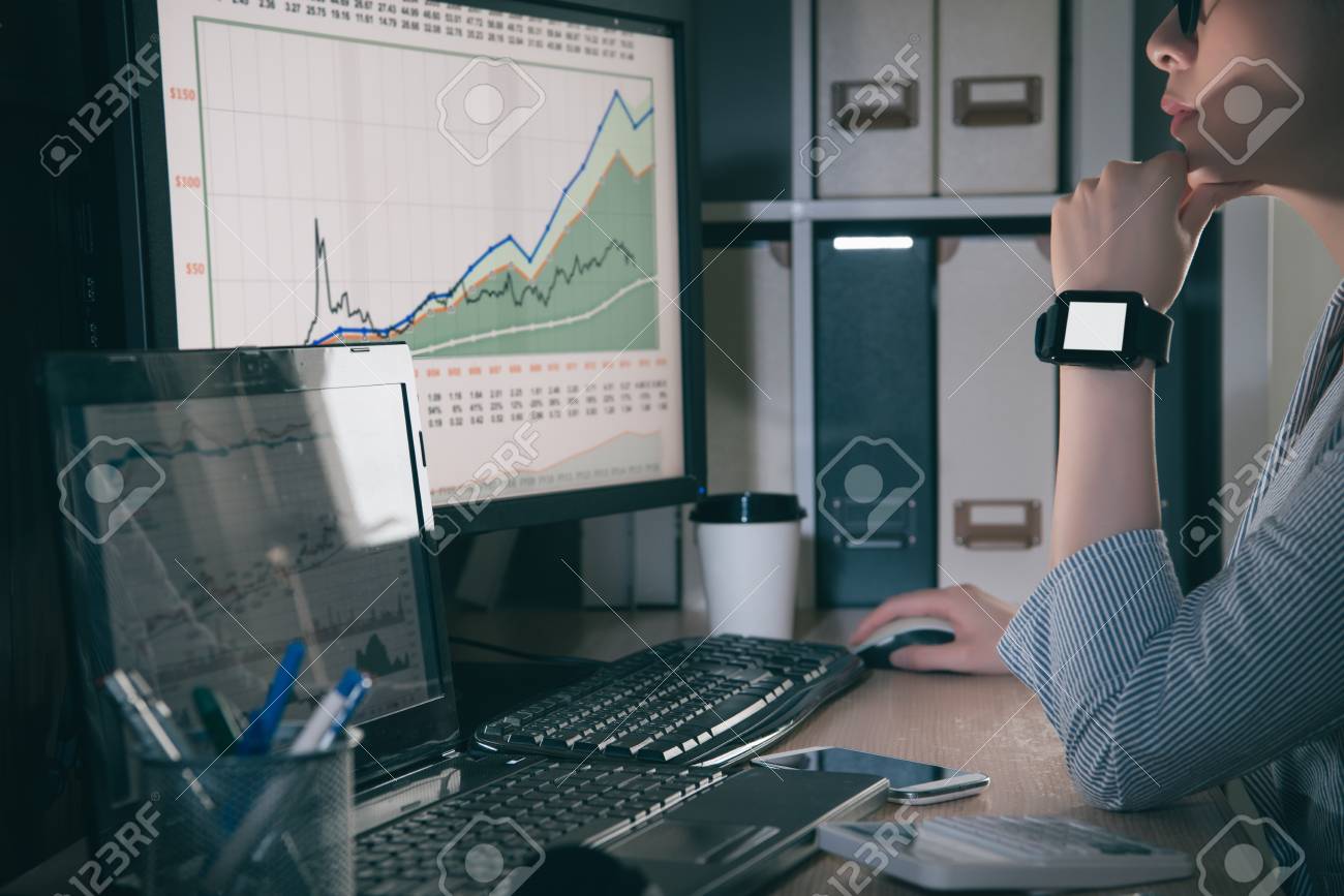 新しい株価チャートを探しています 物思いにふける彼女の職場に座ってあごに手を維持し メガネ着用スマートウォッチの若くてきれいな女性 の写真素材 画像素材 Image