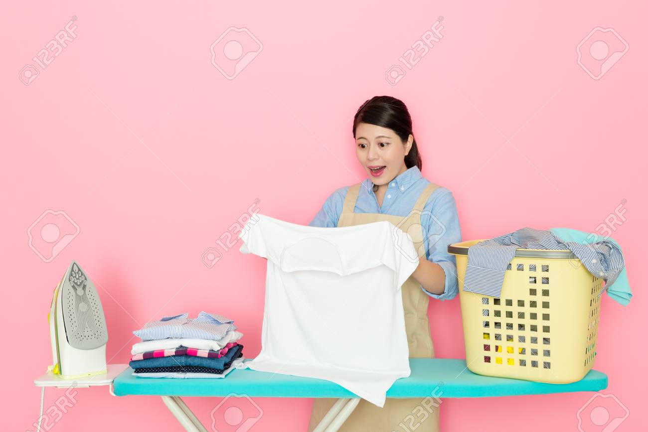 白い服を見て陽気なかわいい女性の主婦は 彼女がピンクの背景アイロンで立っているときに驚いた感じをきれいにした汚れを発見します の写真素材 画像素材 Image