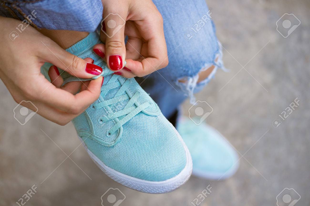 Female hands with a red manicure knotted laces on sports shoes. Young woman in blue jeans walking outdoors when she untied shoelace. A walk in the city. - 43196144 Female hands with a red manicure knotted laces on sports shoes. Young woman in blue jeans walking outdoors when she untied shoelace. A walk in the city. - 43196144