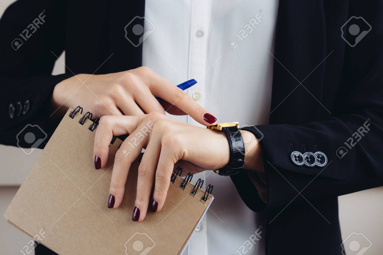 女性ビジネス スーツとえんじ色のノートを保持しているマニキュアし 彼の時計のクローズ アップを見て の写真素材 画像素材 Image