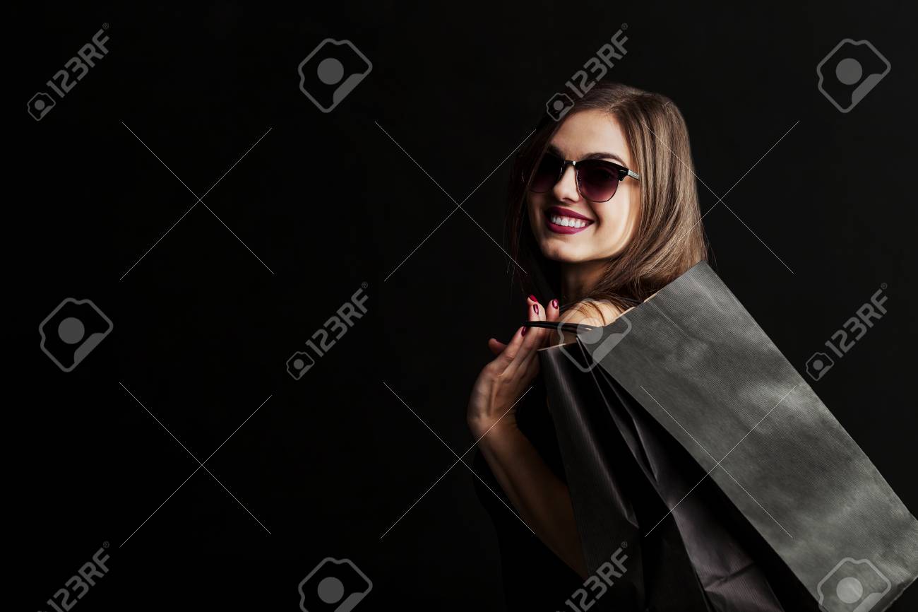 Elegant brunette woman wears sunglasses and black dress holding black shopping bags, black friday concept - 89135962 Elegant brunette woman wears sunglasses and black dress holding black shopping bags, black friday concept - 89135962