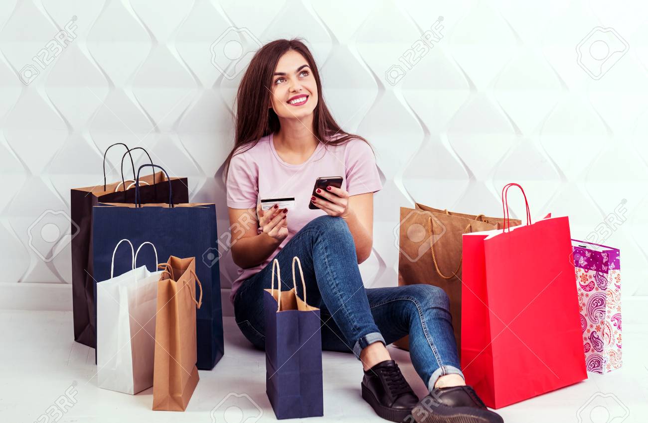 Happy Cheerful Girl Sitting On The Floor With Colorful Shopping