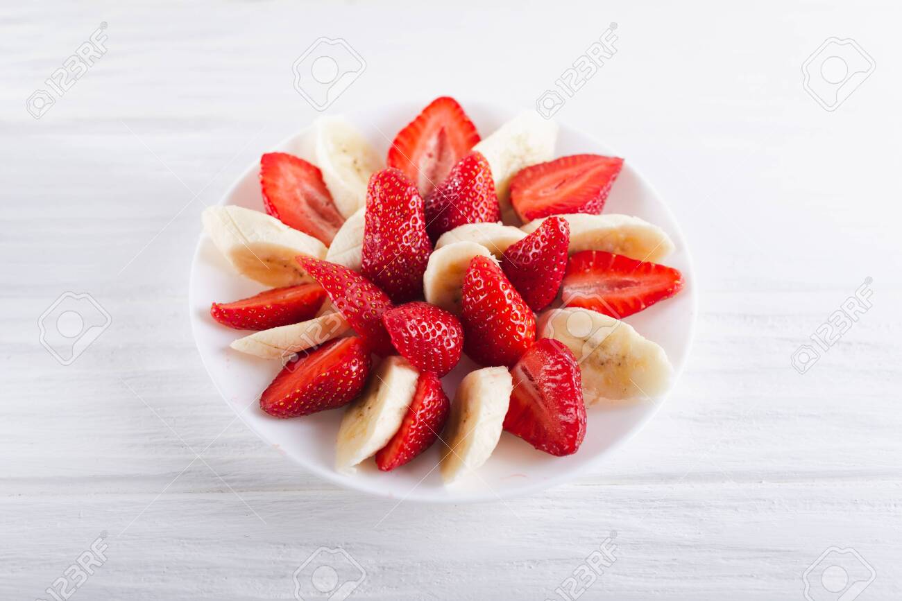 Juicy fresh sliced strawberries with banana on a white plate on a white wooden background. - 151404076 Juicy fresh sliced strawberries with banana on a white plate on a white wooden background. - 151404076